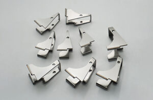 Scattered small stainless steel L-shaped mounting cleats on a grey background