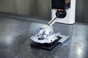 Coordinate measuring machine probe checking a fixtured metal part on a granite table